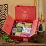 Hộp quà Tết 2 cánh đỏ mở ra, rượu vang, sô-cô-la, bánh quy thiếc, hũ hạt; túi đỏ ép kim