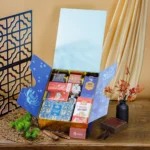 Hộp quà Tết 2 cánh xanh lam mở, lòng ánh kim vàng đựng bánh quy thiếc, trà, kẹo, bánh bơ