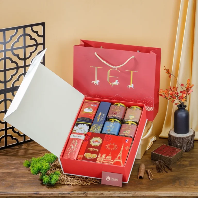 Hộp quà Tết nắp trắng thân đỏ mở ra, xếp trà thiếc, bánh quy, hũ mứt; túi đỏ phía sau